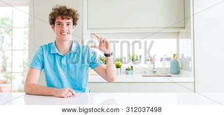 Wide shot of young handsome man at home smiling and confident gesturing with hand doing size sign with fingers while looking and the camera. Measure concept.