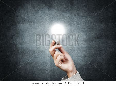 Human Hand With Glowing Incandescent Lamp On Background Grunge Wall. Professional Business Assistanc