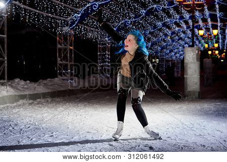 Girl With Blut Hair Skating On The Ice Arena In The Evening City Square In Winter