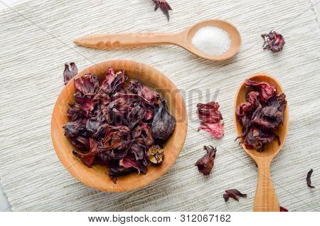 Top View At Wooden Bowl And Spoon Of Dry Hibiscus Petals On Linen Cloth Background