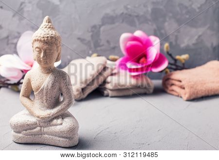 Spa Setting With Decorative Buddha, Towels  And Pink Magnolia Flowers On Grey Textured Background.  