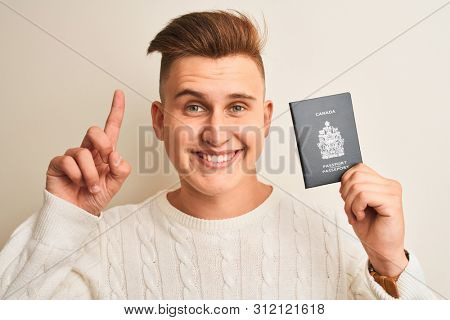 Young handsome man holding Canada Canadian passport over isolated white background surprised with an idea or question pointing finger with happy face, number one