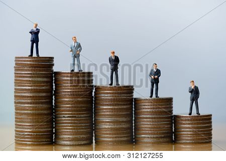 Small Businessmans Figures Standing On Tstack Of Coins. Time Is Money. Time Investment And Retiremen