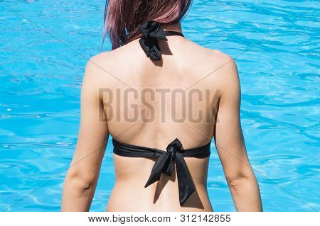 Naked Back Of A Young Woman Against The Blue Water By The Pool. Safety Sunbathing Concept. Copy Spac