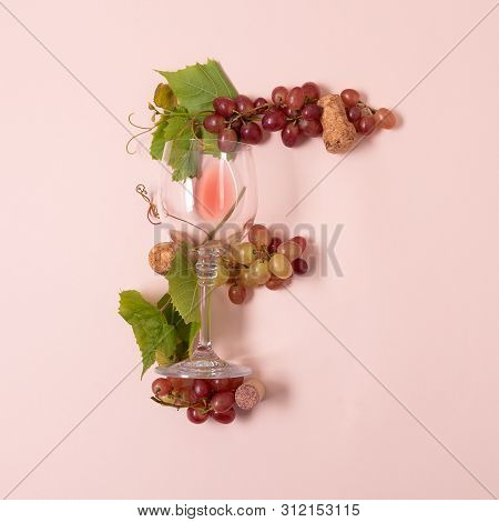 Alphabet. Letter F Made Of Wineglasses With Rose And White Wine, Grapes, Leaves And Corks Lying On P