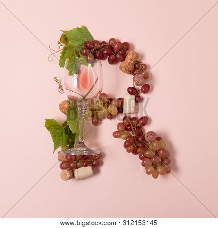 Alphabet. Letter R Made Of Wineglasses With Rose And White Wine, Grapes, Leaves And Corks Lying On P