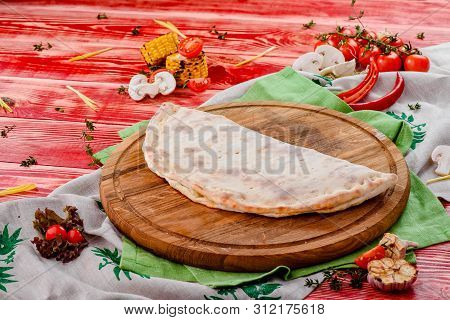 Half Of The Baked Calzone - Closed Type Of Pizza That Is Folded In Half, On A Round Wooden Board On 