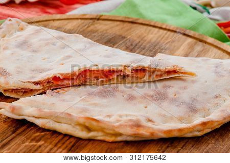 Half Of The Baked Calzone - Closed Type Of Pizza That Is Folded In Half, On A Round Wooden Board On 