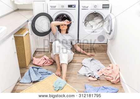 Sad Woman Sitting In Laudry Room With A Pile Of Dirty Clothes
