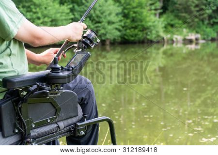 Closeup Of A Man In A Electric Wheelchair Fishing At The Beautiful Pond In Natue On A Sunny Day
