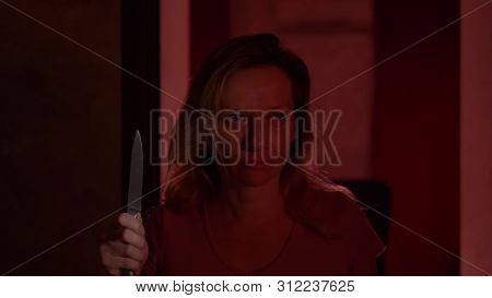 A Woman Experiences Fear And Panic, Walking Along A Dark Corridor With A Knife. Horror Maniac Concep