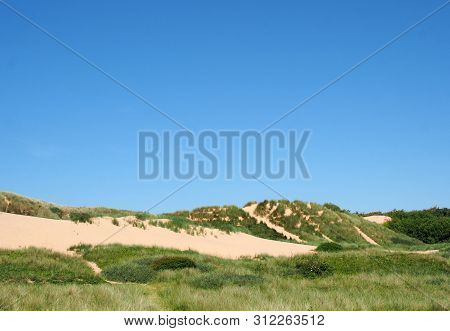 Paths Through Tall Grass Covered Sand Dune Landscape In Front Of The Sea And Bright Blue Sea In Summ