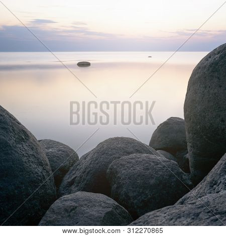 Large Stones On The Background Of The Sea At Sunset Tonted With Orange.