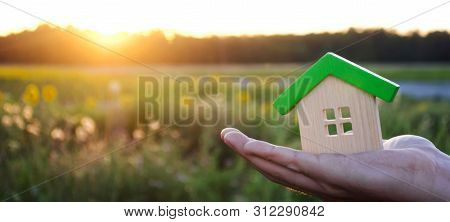 Wooden House In The Hands In The Sunset Background. Real Estate Concept. Eco Friendly Home. Symbol O