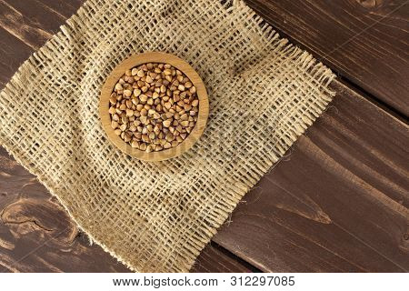 Lot Of Whole Raw Brown Buckwheat Grain In A Wooden Bowl On Jute Cloth Flatlay On Brown Wood