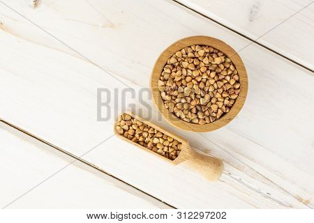 Lot Of Whole Raw Brown Buckwheat Grain In A Wooden Bowl With Wooden Scoop Flatlay On White Wood