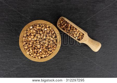 Lot Of Whole Raw Brown Buckwheat Grain In A Wooden Bowl With Wooden Scoop Flatlay On Grey Stone