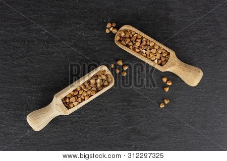 Lot Of Whole Hulled Raw Brown Buckwheat Grain With Wooden Scoop Flatlay On Grey Stone