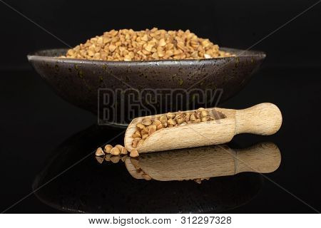 Lot Of Whole Raw Brown Buckwheat Grain In A Grey Ceramic Bowl With Wooden Scoop Isolated On Black Gl
