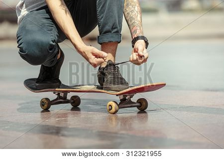 Skateboarder Preparing For Riding At The Citys Street In Sunny Day. Young Man In Sneakers And Cap Wi