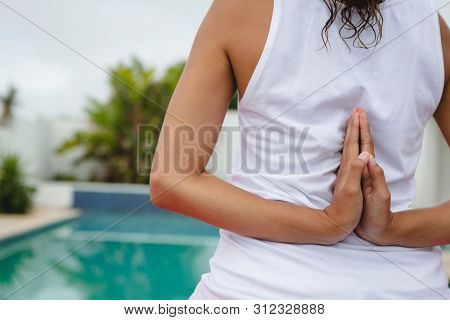 Mid section close-up of mixed-race woman performing yoga near swimming pool in the backyard. Summer fun at home by the swimming pool