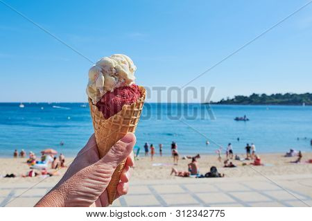 Hand Is Holding Ice Cream Cone In Front Of A Beach In Brittany, France