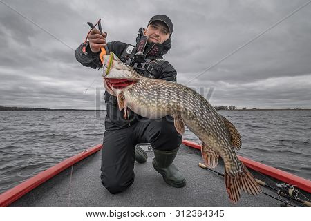 Pike Fishing. Happy Fisherman With Big Fish Trophy At The Boat With Tackles