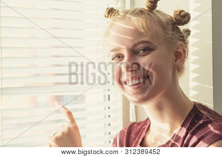 Fun Shy Young Woman Near Window Blinds Looking At Camera Smiling