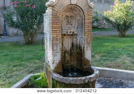 Old Drinking Fountain With Stylized Face And Flowing Water In The Park. Rome, Italy