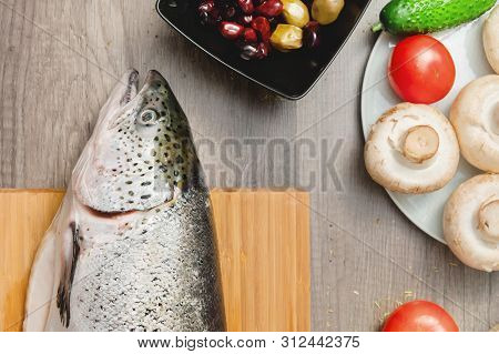 Close-up Keta Fish, Whole On The Cutting Board Of The Kitchen Table Next To Olives Tomatoes And Mush