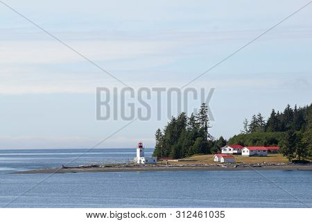 Inside Passage, Canada - August 5, 2006 - Lighthouse And Red-roofed Buildings With Evergreen Forest 