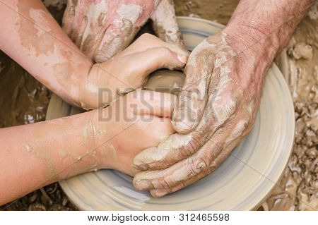 Two Pairs Of Hands Mold Something From Clay On A Potter's Wheel