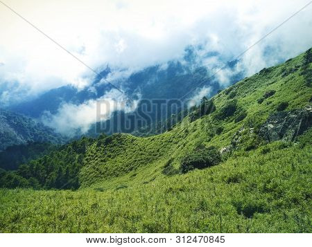 White Clouds On A High Mountains With Green Field. Smoky Fog Filling Valley Between Two Hills. Contr