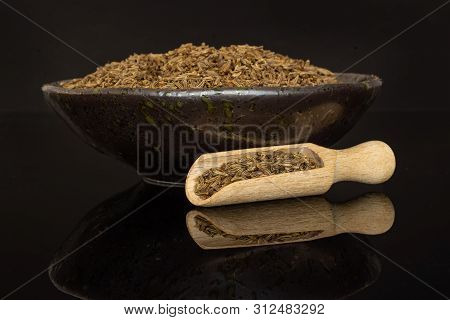Lot Of Whole Dry Caraway Fruits In A Grey Ceramic Bowl With Wooden Scoop Isolated On Black Glass