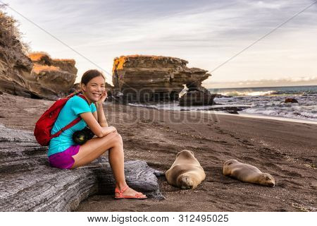 Portrait of woman tourist smiling happy looking at camera on Galapagos Islands sitting by Sea Lions on Galapagos adventure travel with cruise ship, Puerto Egas (Egas port) Santiago island, Ecuador.