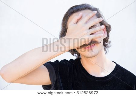 Smiling Young Man With Mustache Covering Face With Hand. Stylish Guy Wearing Velvet T-shirt Posing. 
