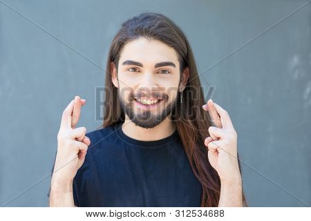 Smiling Young Bearded Man With Piercing Holding Cross Fingers. Stylish Brunet With Long Hair And Pie