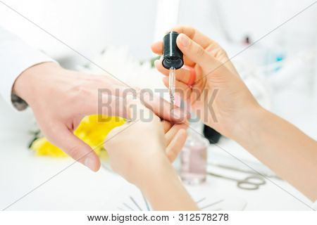 Experienced manicurist pouring oil on finger nails of man after manicure