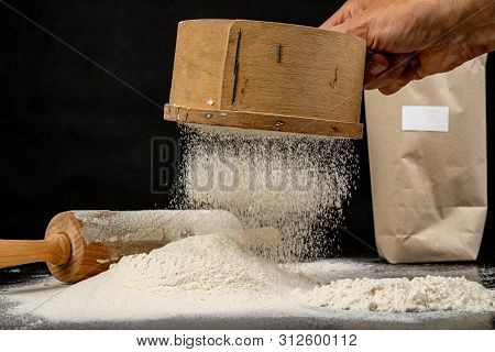 Flour Sifted Through An Old Wooden Sieve. Accessories In Home Kitchen On A Dark Table.