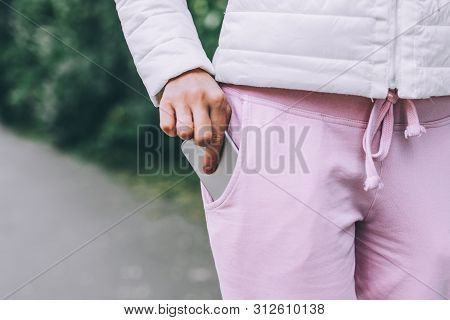 Close Up Of Womans Hand In White Jacket Put Grey Smartphone In Her Not Zippered Pocket On Pink Sport