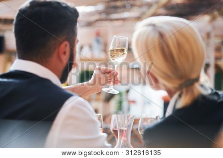 Two professional cavists studying characteristics of wine sample in flute