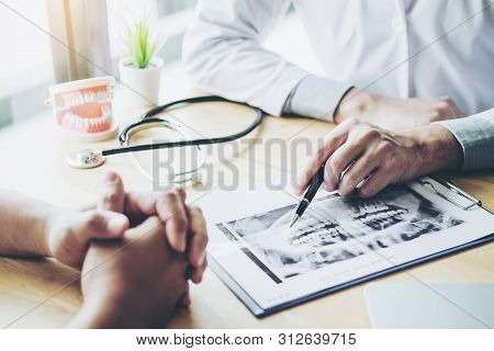 Dentist Talking To Male Patient And Presenting Results On Dental X-ray Film About The Problem Of The