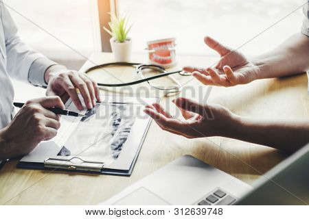 Dentist Talking To Male Patient And Presenting Results On Dental X-ray Film About The Problem Of The