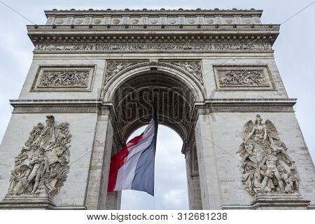 Front View Of Arc De Triomp With Flag Of France Waving In Wind On Place De Gaulle In Paris, France