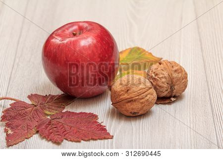 Apple, Walnuts And Dry Leaves On Gray Wooden Boards. An Autumn Still Llife.