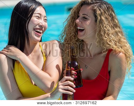 Caucasian Girl And Oriental Girl Play And Laugh In The Pool, Drinking Beer