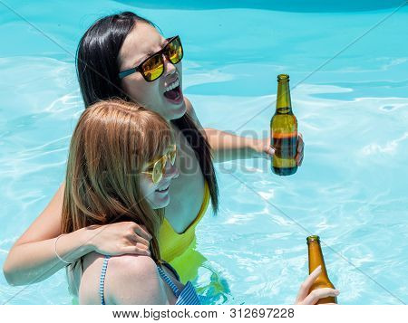 Caucasian Girl And Oriental Girl Play And Laugh In The Pool, Drinking Beer