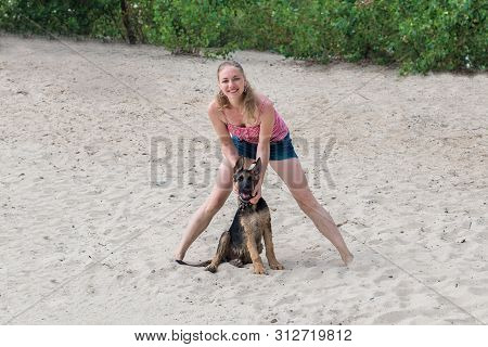 Happy German Shepherd Puppy And Beautiful Blonde Girl Have Fun Running On The Beach And Playing On T