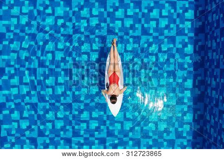 Top View Of Woman In Bikini Is Sunbathing On A Surfboard In Pool, Aerial View. Girl Travel And Explo