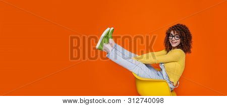 Cute Curly Haired Hipster Woman Wearing In Green Shoes Sitting On Chair With Funny Raised Legs